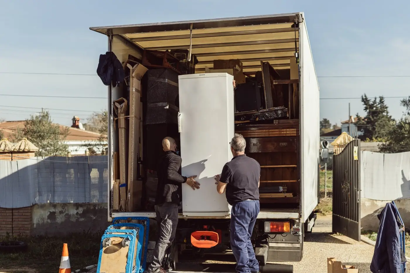 Two workers loading a refrigerator into a box truck for removal